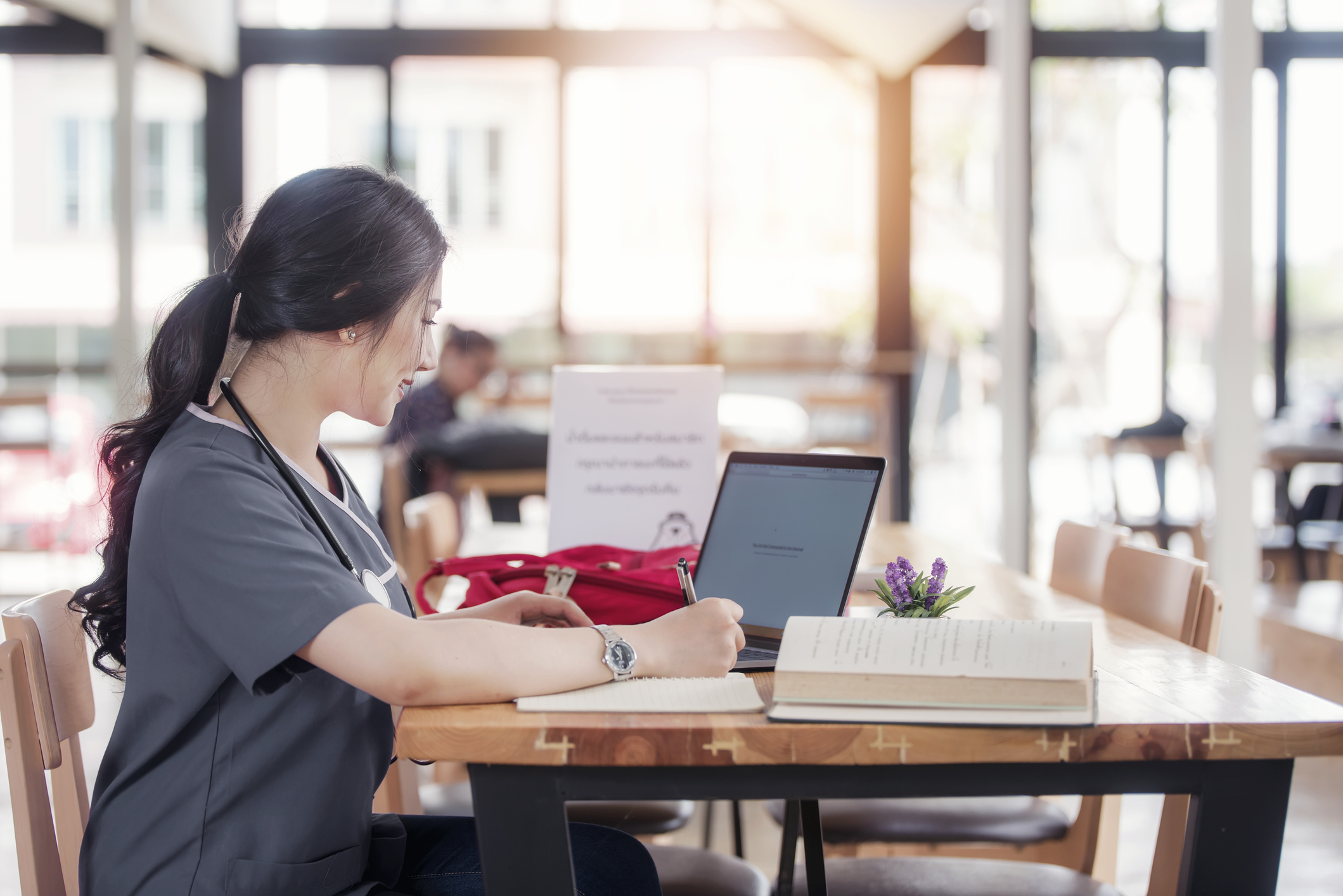 Eine Frau in grauer Funktionskleidung einer Klinik sitzt an einem Laptop und schreibt.